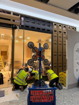 The MFC 750 Mini Floor Crane and GGR800+ Glass Vacuum Lifter lifting shopfront glazing at Heathrow Airport.