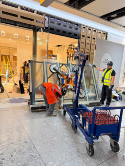 The MFC 750 Mini Floor Crane and GGR800+ Glass Vacuum Lifter lifting shopfront glazing at Heathrow Airport.
